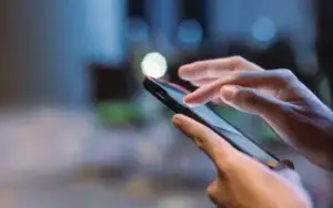 Shopify-Address-Validation-Ireland | Autoaddress | Autoaddress Close-up of hands using a smartphone, finger tapping the touchscreen in a dim, blue-toned outdoor setting