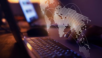 An image displaying several laptops opened and arranged on a table, with a large, detailed world map spread out beneath them. The laptops' screens are visible, suggesting they are being used for global communication or international business purposes. The map and laptops together symbolize the theme of global connectivity and the importance of digital tools in facilitating international interactions.