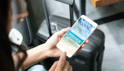 The image shows a person engrossed in using their smartphone, presumably booking a holiday through a travel agent. They appear focused and engaged, symbolizing the modern traveler’s reliance on digital platforms for travel planning and the importance of efficient and accurate address capture in enhancing their booking experience.