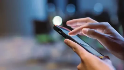 Close-up of hands using a smartphone, finger tapping the touchscreen in a dim, blue-toned outdoor setting