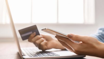 A dynamic image capturing a shopper completing an online purchase on a desktop, with a mobile phone and credit card in hand. This scene illustrates the ease and security of the e-commerce checkout process, enhanced by Autoaddress's streamlined address capture and verification solutions.
